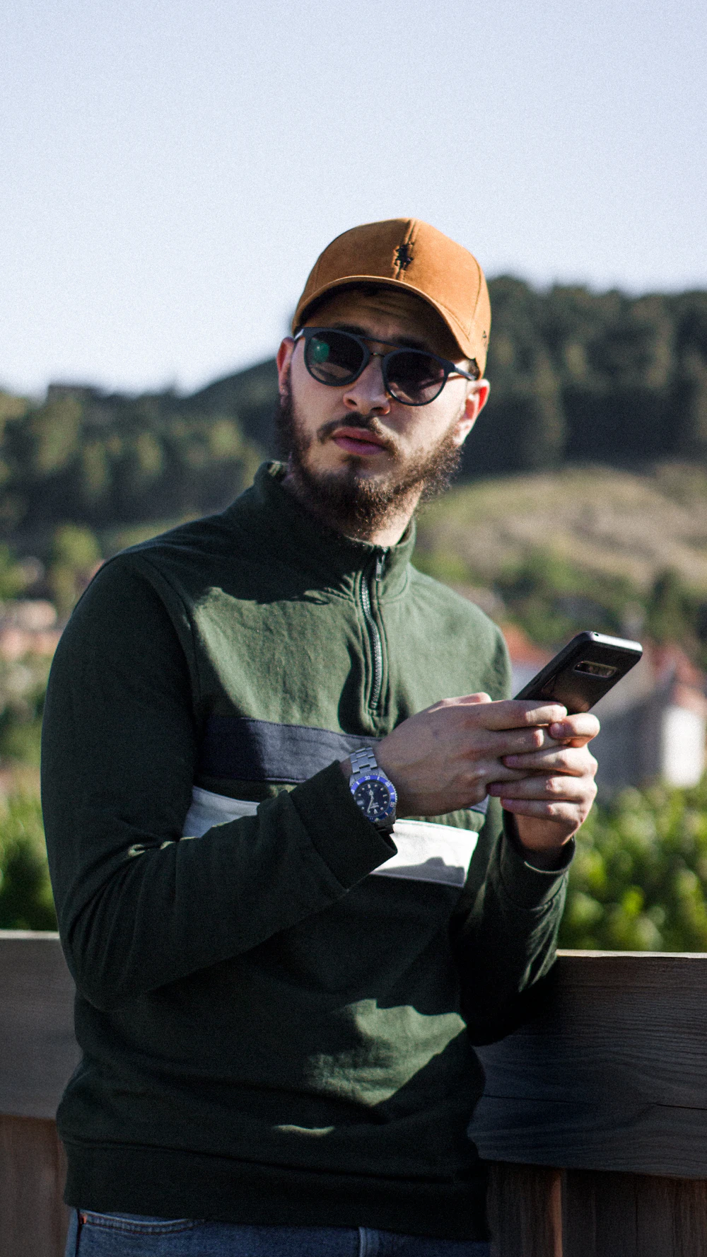 Man in a green casual jacket holding his phone outdoors