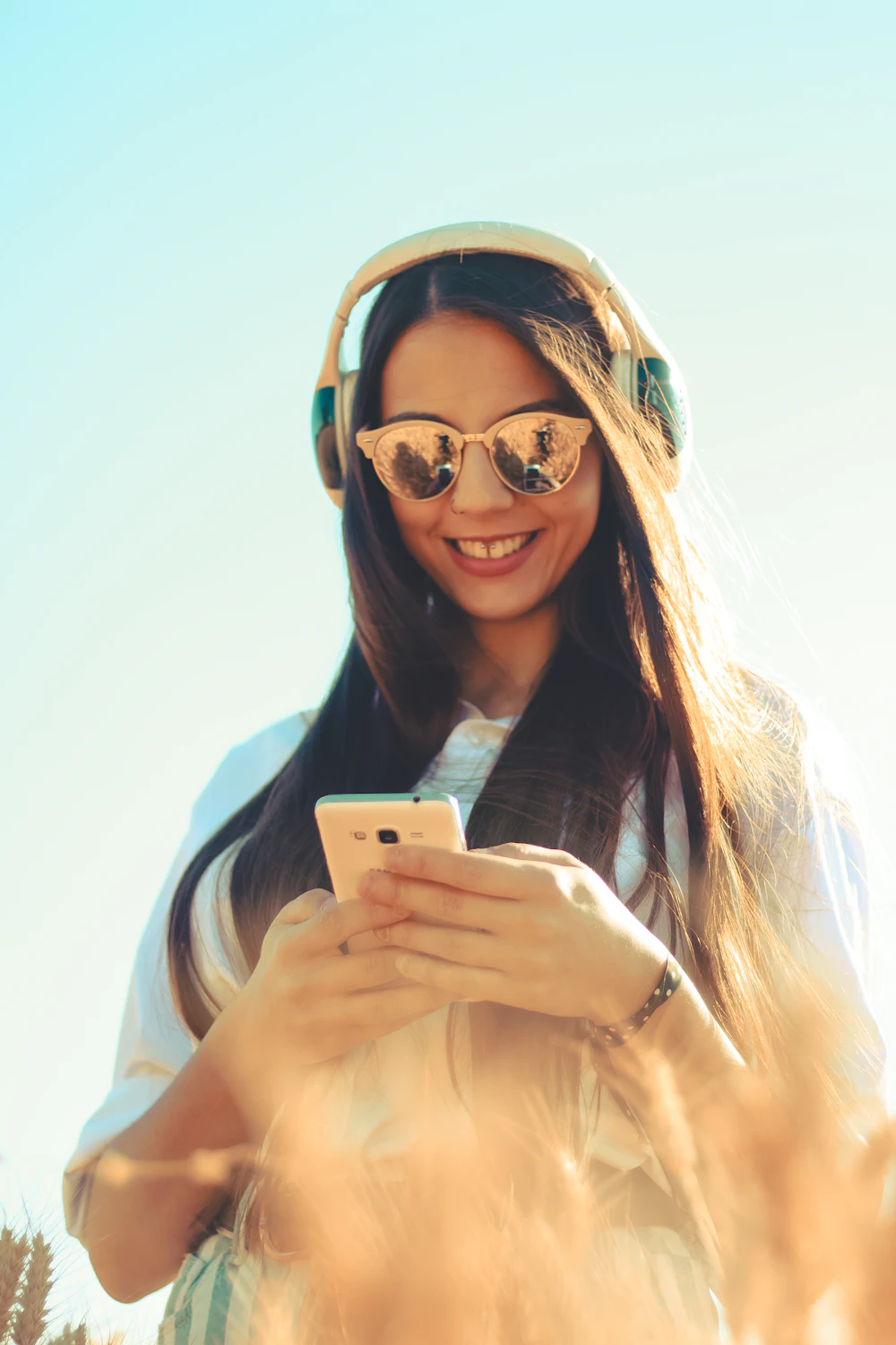 Woman standing outdoors in casual clothes, smiling while using her phone
